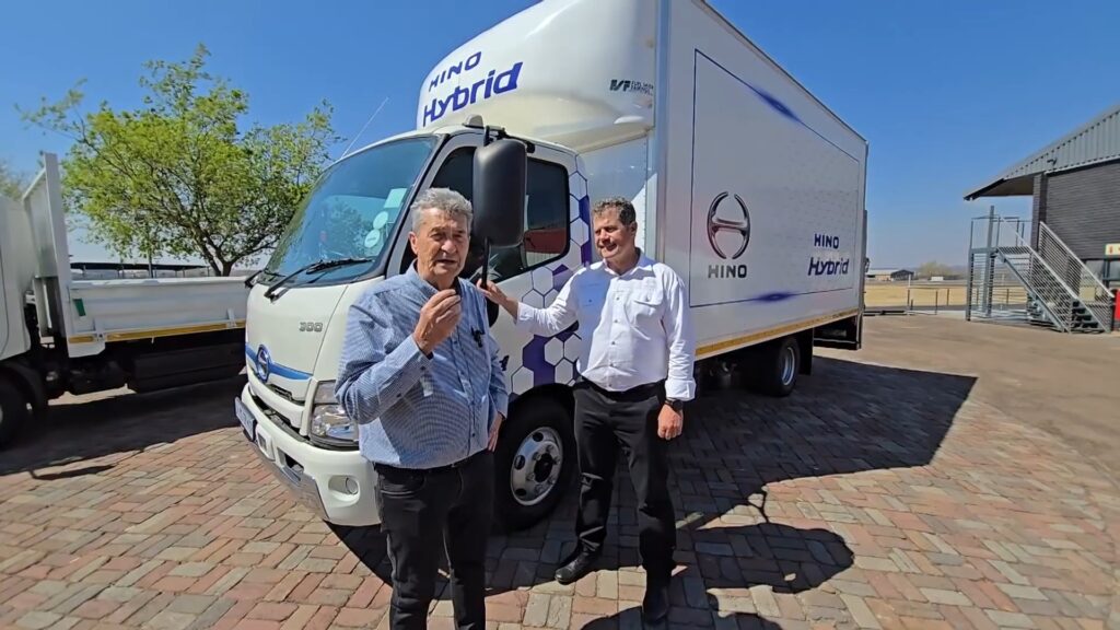 Two men beside Hino hybrid truck outdoors.