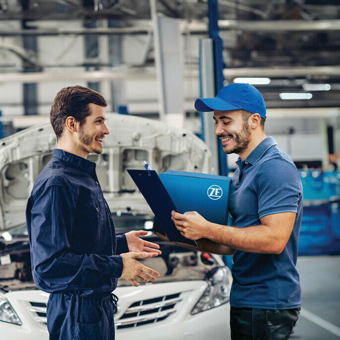 Two mechanics discussing vehicle repair with clipboard.